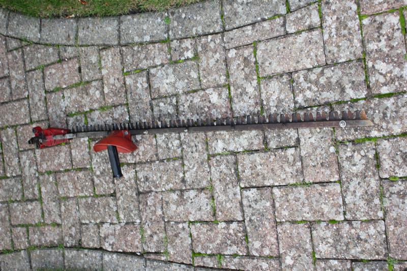 Long-reach hedge cutting attachment with red motor head laid across block paving.