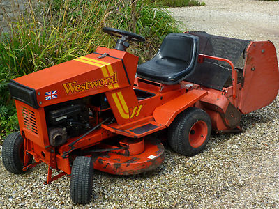 Orange Westwood ride-on mower parked on gravel beside planting.